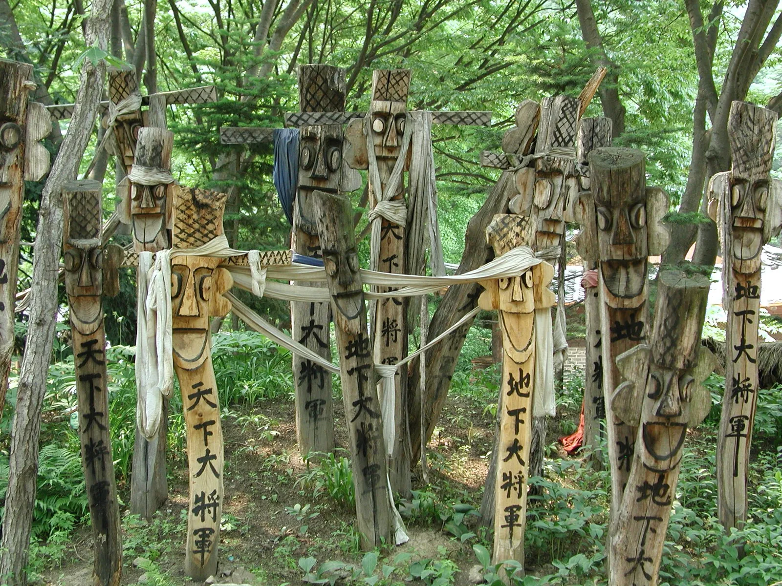 Carved jangseung village guardian posts in the woods at the Korean Folk Village