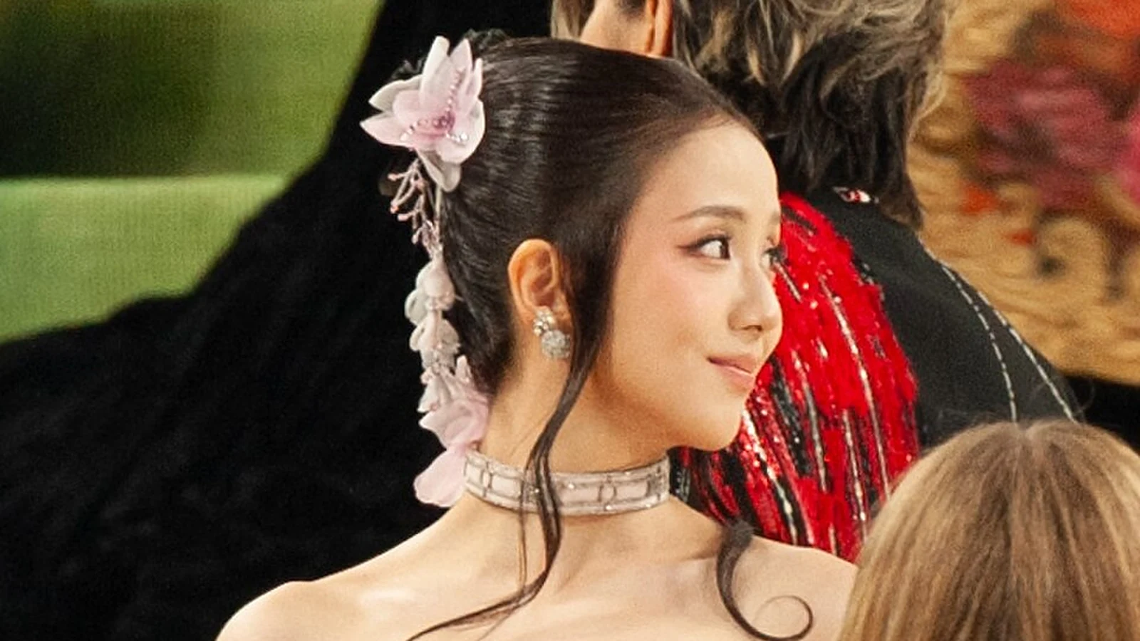 JISOO smiling over her shoulder in a pink floral hair piece and choker at the 2026 Met Gala. Photo: SWinxy via Wikimedia Commons, CC BY 4.0