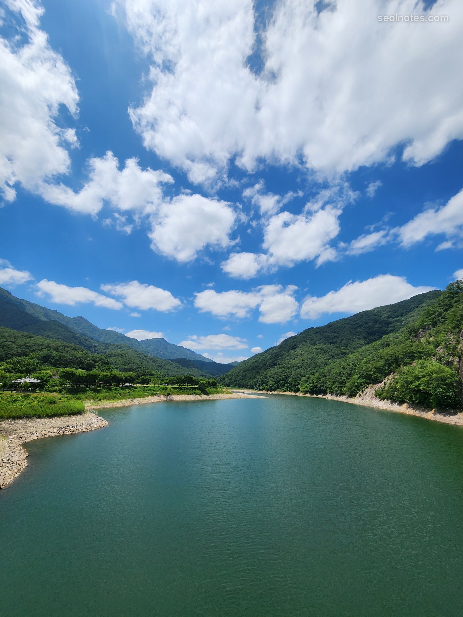 Green reservoir between forested mountains under big white clouds
