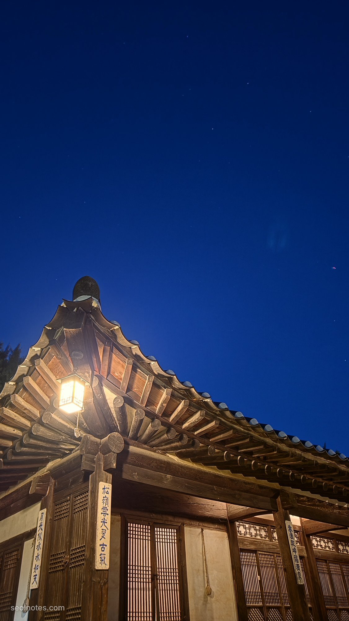 A lit hanok roof under a deep blue evening sky